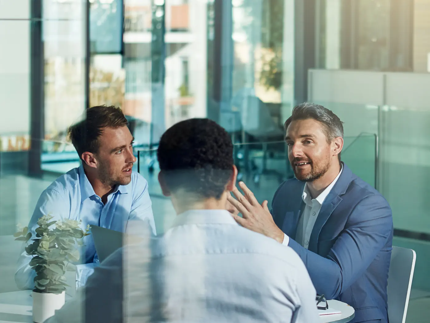 Three executives in conversation around a table in a glass-walled office